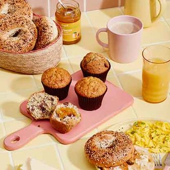 Breakfast spread with bagels, muffins, coffee, orange juice, and scrambled eggs.