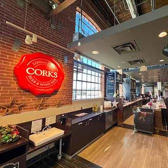 Interior of Corks Beer & Wine Bar with exposed brick wall, red Corks sign, and modern counter setup.