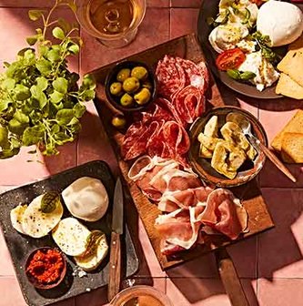 Italian charcuterie items including proscuitto, roasted peppers and cheese on various wood and slate boards.