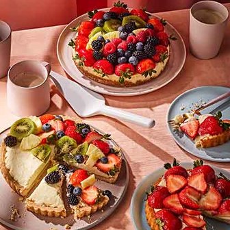 Fruit-topped tarts with strawberries, kiwi, and berries on plates and cups.