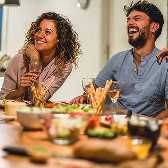 Two people sitting at a table with wine glasses and assorted appetizers.