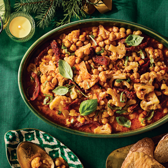 Chickpea and cauliflower stew with peas and herbs in a tomato-based sauce on a green platter.