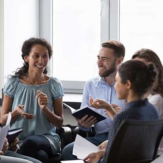 Group of people seated in a circle holding notebooks and papers, engaged in discussion.