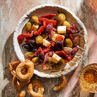 Antipasto plate with mixed olives, sun-dried tomatoes, cheese cubes, cured meats, and taralli crackers.