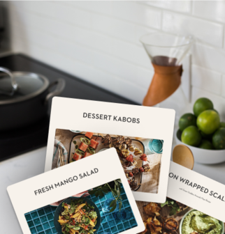 Recipe cards for dessert kabobs, fresh mango salad, and bacon-wrapped scallops displayed in a kitchen setting.