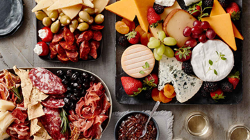 Charcuterie boards with assorted cheeses, meats, olives, fruit, and crackers.