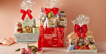 Three gift baskets wrapped in clear cellophane with red bows and gourmet items.