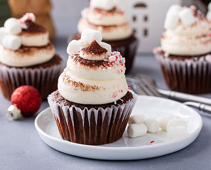Chocolate cupcake topped with creamy frosting, cocoa dust, crushed peppermint, and mini marshmallows on a white plate.
