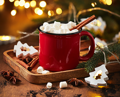 Festive red mug of hot chocolate topped with marshmallows and cinnamon sticks on a wooden tray with holiday decor