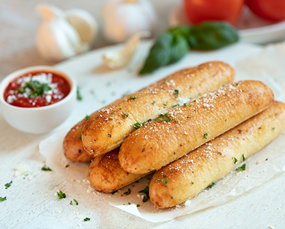 Golden garlic breadsticks sprinkled with herbs and Parmesan, served with marinara sauce on a white board.