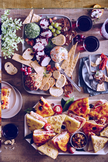 Assorted catering spread with pizza, charcuterie, bread, and dips on a table, ideal for graduation and celebration catering.