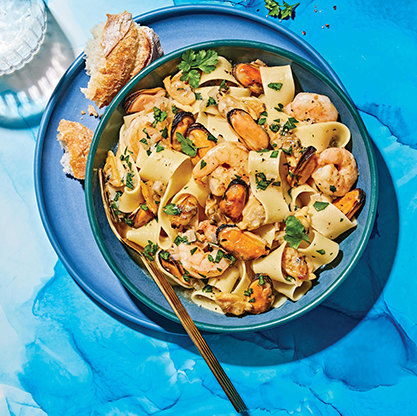 Seafood pasta with shrimp and mussels in a light sauce, served with bread on a blue plate.
