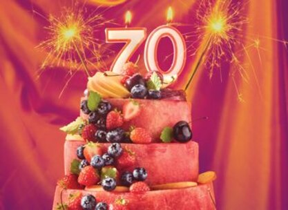 Festive watermelon fruit cake topped with fresh berries and a sparkling 70th birthday candle celebration.