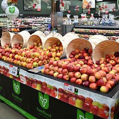 Display of fresh apples in wooden baskets at a Foodland grocery store produce section.