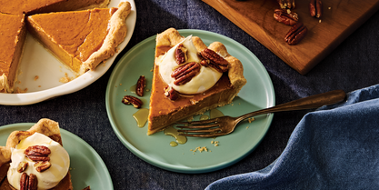 Slice of pumpkin pie topped with whipped cream, pecans, and maple drizzle on a dessert plate.