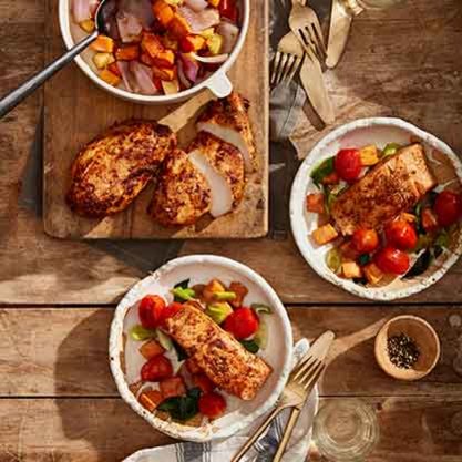 Two plates of salmon with roasted vegetables and a cutting board with sliced chicken and a bowl of mixed vegetables.