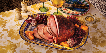 Glazed holiday ham sliced on a serving platter with grapes, radicchio, and apricots for a festive dinner.