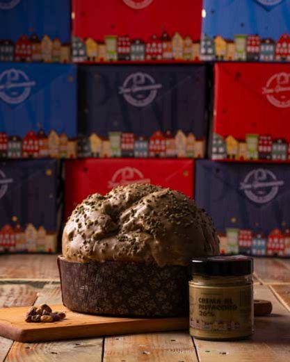 Chocolate-glazed panettone with pistachio spread jar and gift boxes in background.
