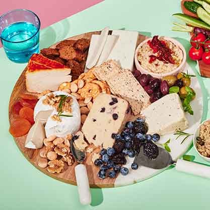 Plant-based charcuterie board with assorted vegan cheeses, nuts, dried fruit, and olives.