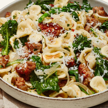 Orecchiette pasta with Italian sausage, rapini, and grated cheese in a white bowl