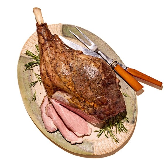 Roasted leg of lamb, sliced and served on a platter with rosemary garnish, ready-to-serve entrée.