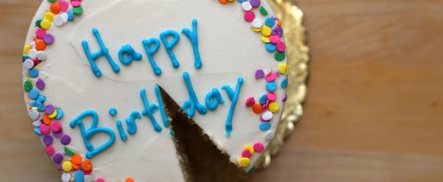 Birthday cake with colorful sprinkles and a slice removed, featuring “Happy Birthday” icing decoration.