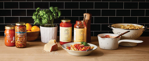 Pasta dish with tomato sauce, jars of sauce, cheese, and fresh basil on a counter.