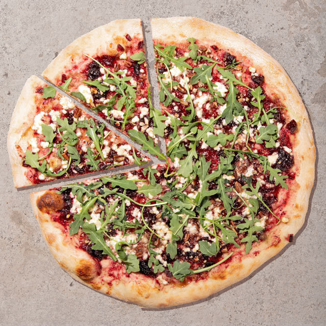 Cranberry arugula pizza topped with feta and fresh greens on a stone surface.
