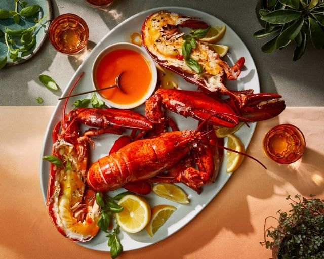 Grilled lobster platter with lemon wedges, butter sauce, and fresh herbs, seafood fine dining dish on elegant plate.