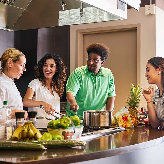 Group of people cooking together in a modern kitchen with fresh fruits and vegetables on the counter.