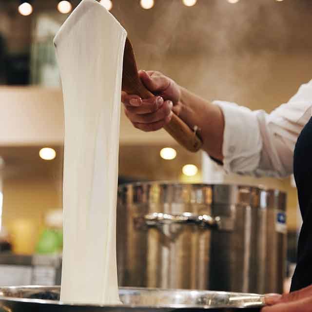 Fresh mozzarella being stretched by hand over a pot during traditional cheese-making.