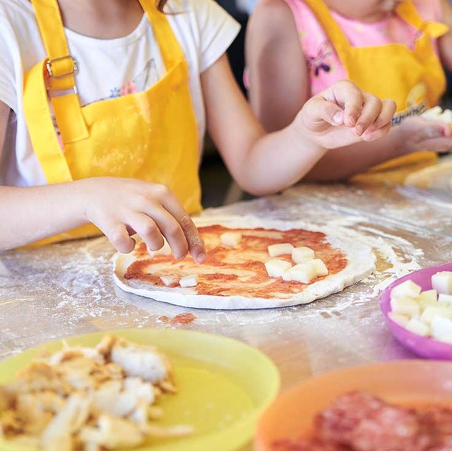 Child adding cheese cubes to a pizza dough with tomato sauce.