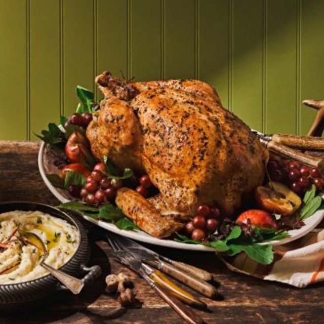 Roast turkey on a platter with grapes, apples, herbs, and mashed potatoes.