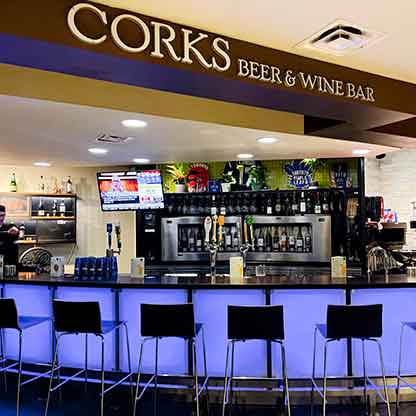 Corks Beer & Wine Bar interior with illuminated counter, bar stools, and shelves of bottles.